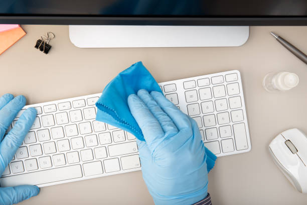 Hand with protective glove cleaning a keyboard with disinfectant. COVID-19 Coronavirus outbreak prevention concept. Top view