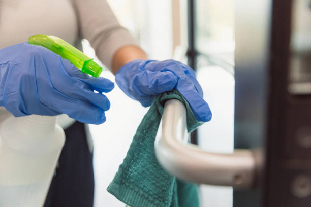 A female custodian wears protective gloves as she cleans a hand rail in an office during COVID-19