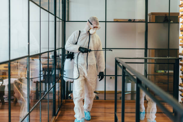 Man in protective suit and face mask spraying for disinfection in the office
